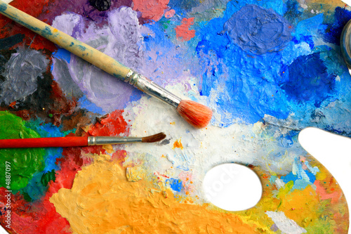 Two Brushes lay on an art palette in bright paints