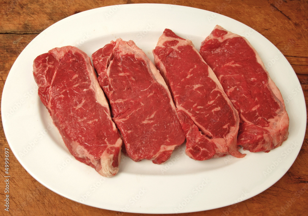 raw New York strip steaks on a platter