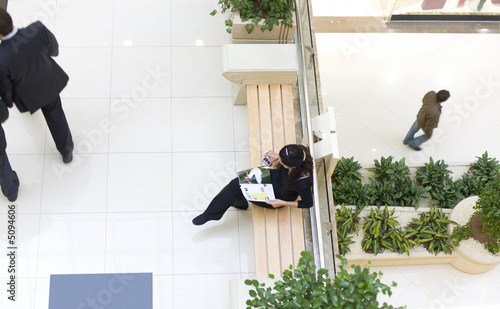 Girl sitting on bench and reading a magazine in a mall