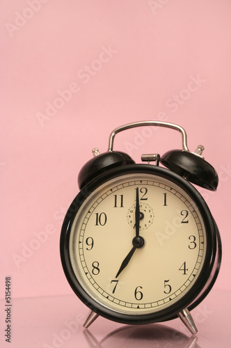 The black alarm clock is on a pink background