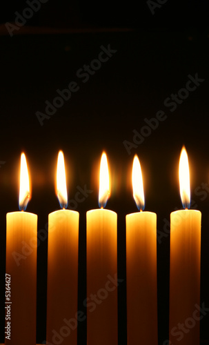 Five burning candles over black background
