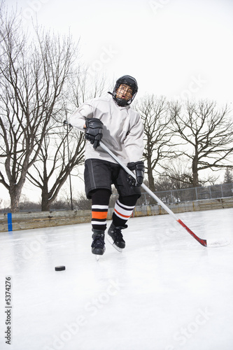 Boy in ice hockey uniform skating on ice rink moving puck.