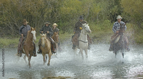 Cowboys on horseback gallop through river.