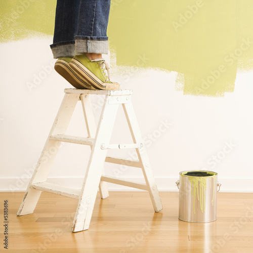 Legs of woman standing on tiptoe on stepladder with paint can. photo