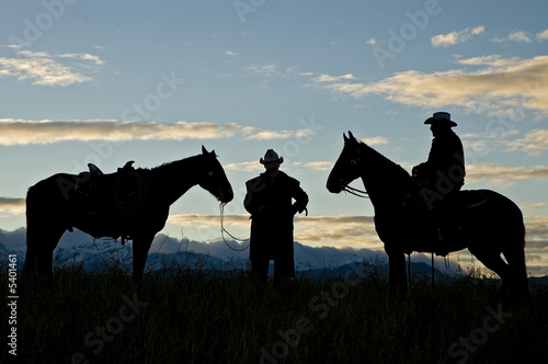Cowboy silhouettes against a dawn sky