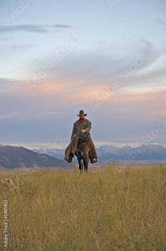 Cowboy riding the range against dawn sky. 