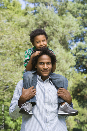 Father carrying son on shoulders in park.