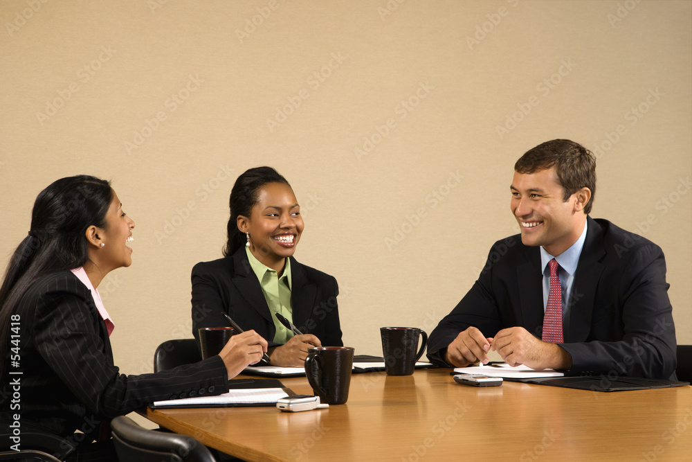 Businesspeople sitting at conference table talking and smiling. Businesspeople sitting at conference table talking and smiling.