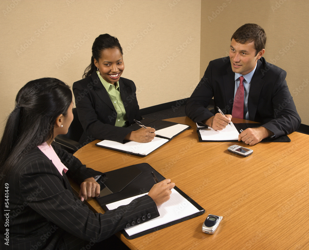 Businesspeople sitting at conference table talking and smiling. Businesspeople sitting at conference table talking and smiling.