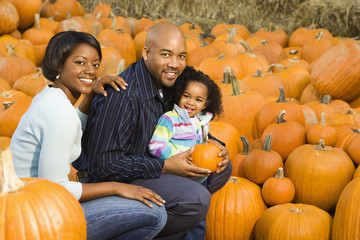 Happy family picking out pumpkin and smiling for fall portrait.