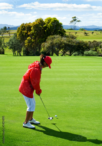Lady in red jacket putting on golf green
