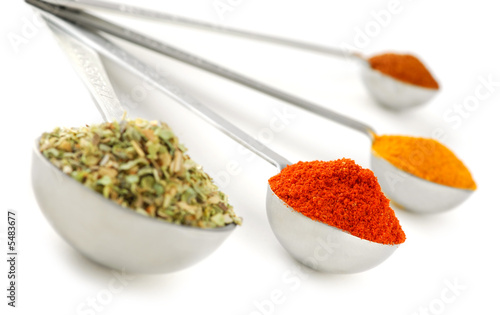 Assorted spices in metal measuring spoons on white background photo