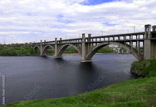 Arch bridge on a dark river with green banks