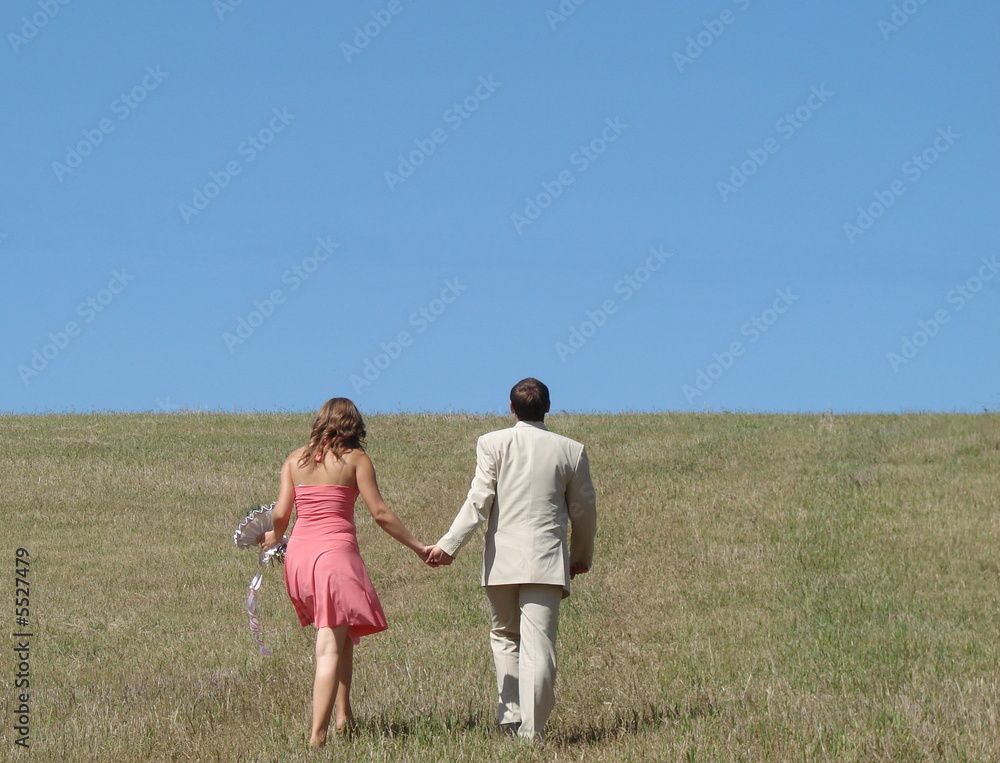 Young couple walking in wide green field under blue sky