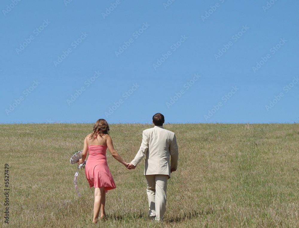 Young couple walking in wide green field under blue sky Young couple walking in wide green field under blue sky