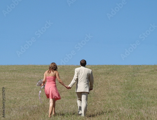 Young couple walking in wide green field under blue sky