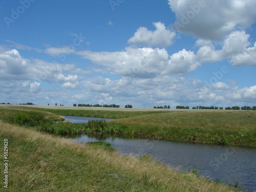 wide summer field with river uder cloudy deep blue sky