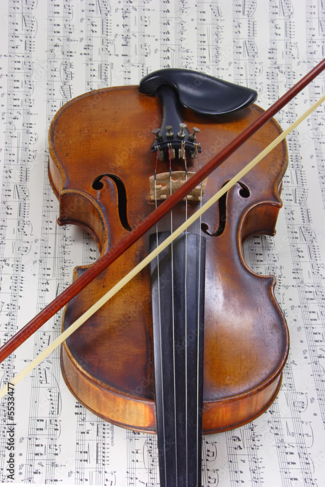 Fototapeta premium Alte Violine mit Bogen mit Noten im Hintergrund
