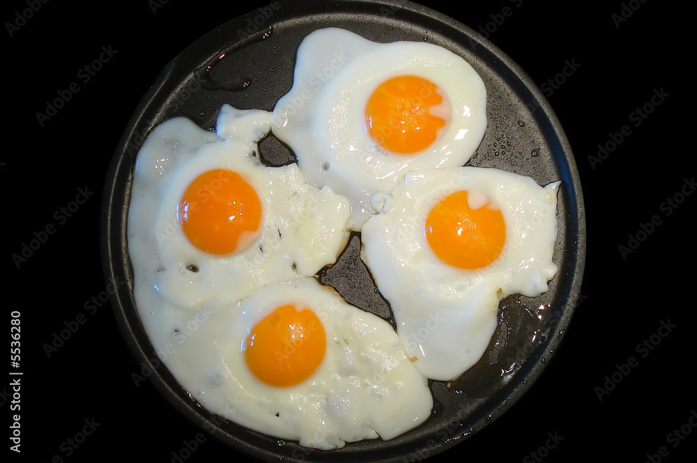 Four fried eggs in a frying pan isolated on black Four fried eggs in a frying pan isolated on black
