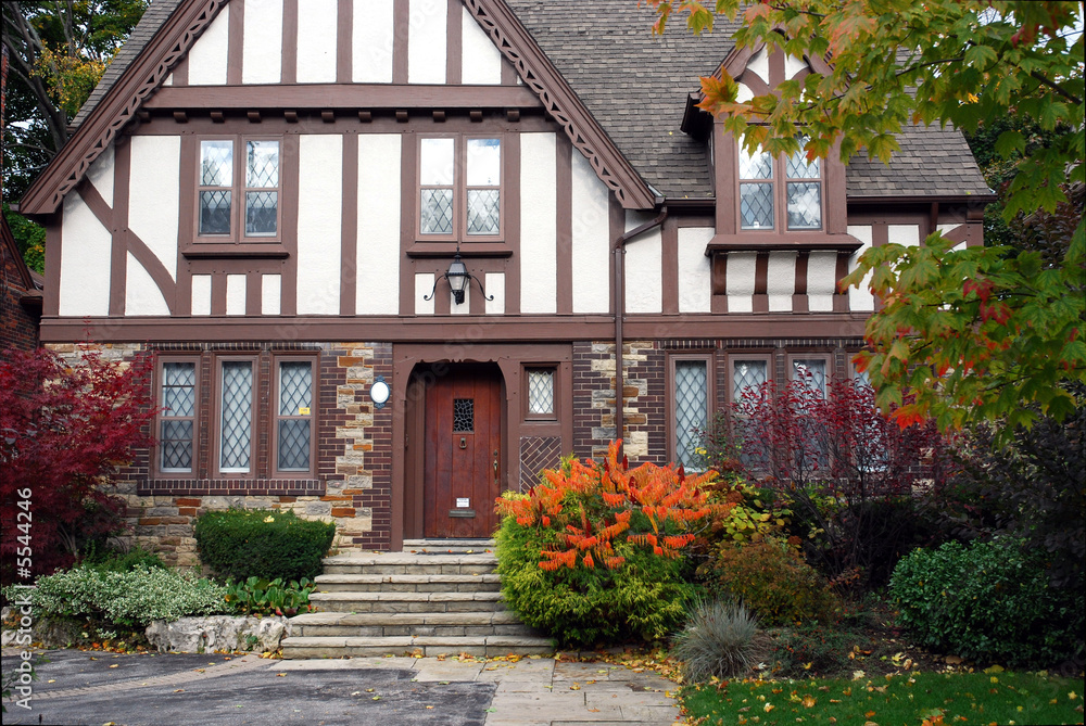 tudor style home with brown trim and sumac bush in fall