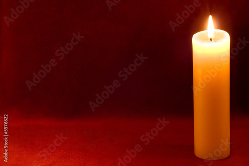 Burning yellow-white candle on scarlet background