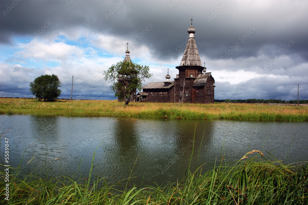 Ancient wooden russian church beyond the river, stormy clouds
