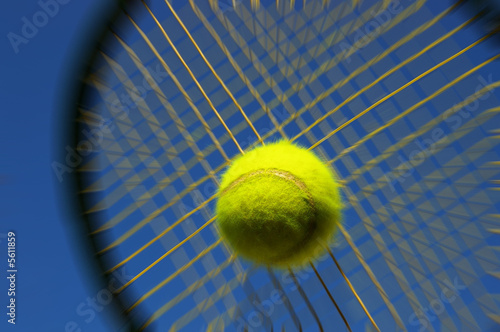 Tennis racket hitting ball against blue sky