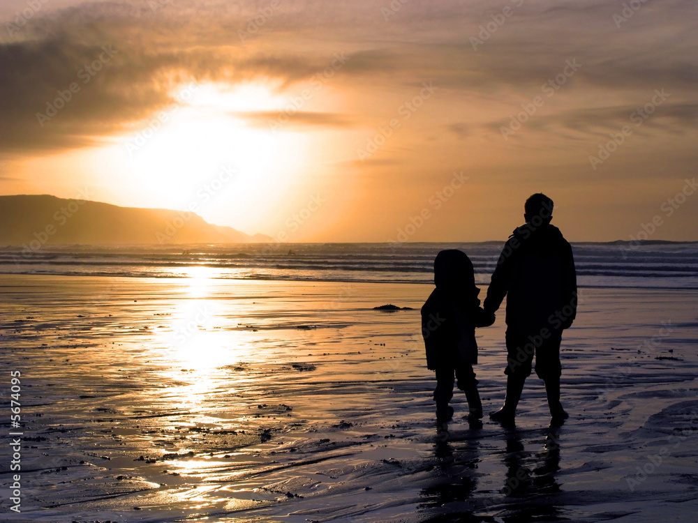 Two children holding hands whilst watching a beach sunset.