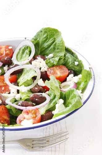 Greek salad in enamel bowl on rustic white timber table