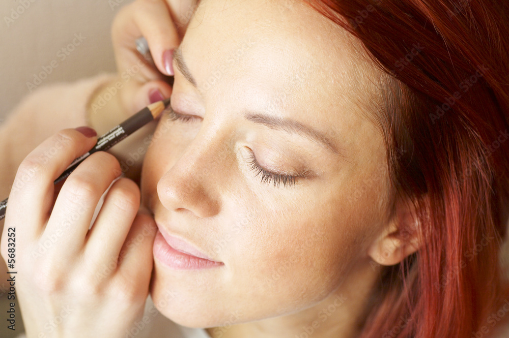 beautician is doing make-up to red-haired woman