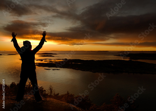 A person standing by the ocean raising their arms in celebration