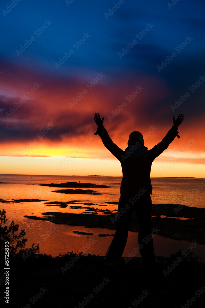 A person standing by the ocean raising their arms in celebration