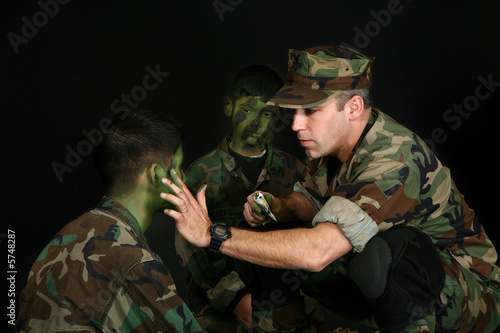 Father puting camo paint on children's faces over black. photo