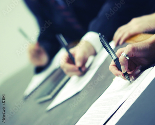 three hands holding pens signing document on table