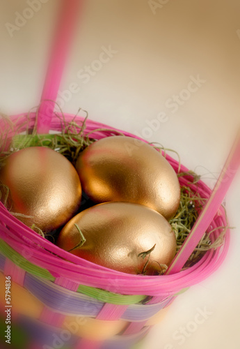 Colorful Easter basket containing 3 golden eggs, blurred edges.