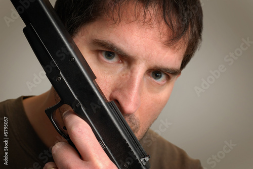 Angry, crazy-looking man holding gun in front of face.