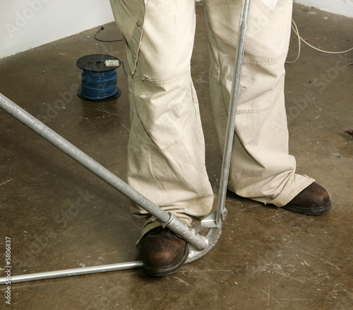 Closeup of electrician's feet as he bends pipe.  