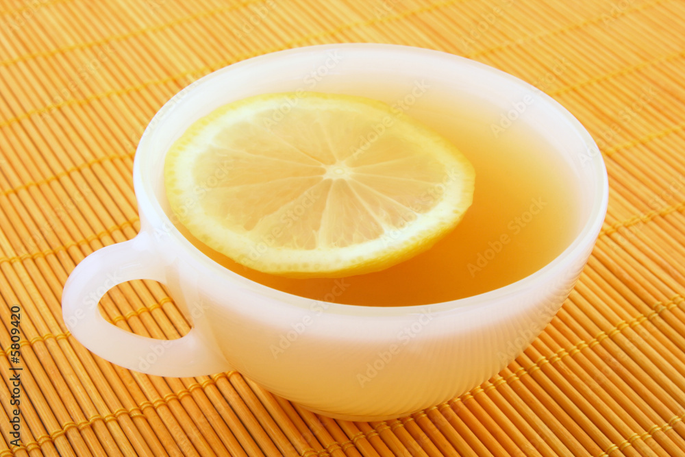 Cup of tea with lemon on a rattan mat in warm golden light. Cup of tea with lemon on a rattan mat in warm golden light.