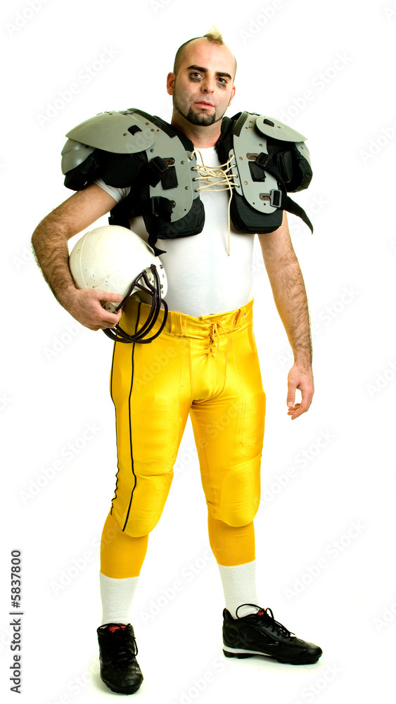 An American football player. Standing, holding helmet.
