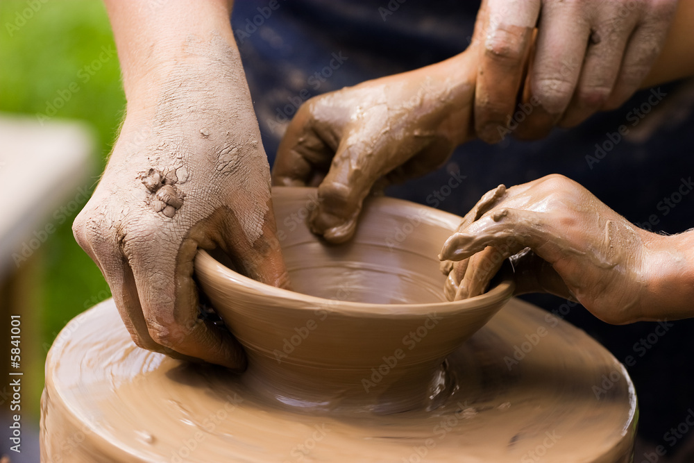 Potters hands guiding a child to help him with the ceramic wheel