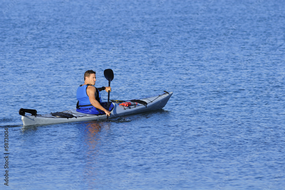 Athletic kayaker rows off into calm blue waters 