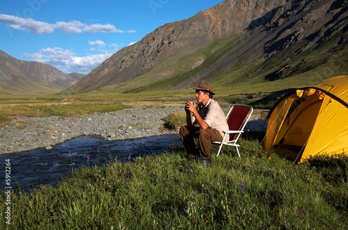 man is drinking at the camp in mountains near the stream © Serg Zastavkin
