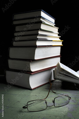 pile of study books with glasses lying in front.  One book open.