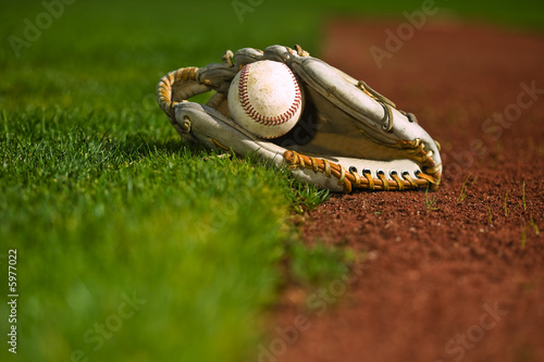 Baseball in a mit sitting on the grass and dirt of a diamond