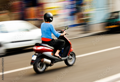 Fotografia Panning shot of a young girl riding a scooter in a European city