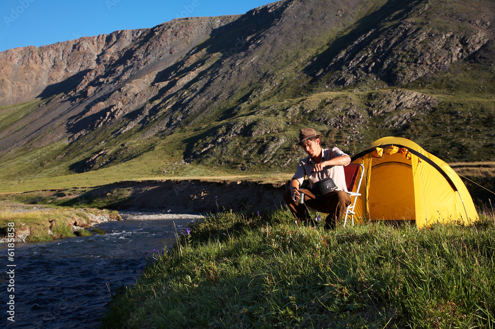 Fototapeta premium man is drinking at the camp in mountains near the stream
