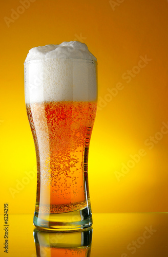 Glass of beer close-up with froth over yellow background #6224295
