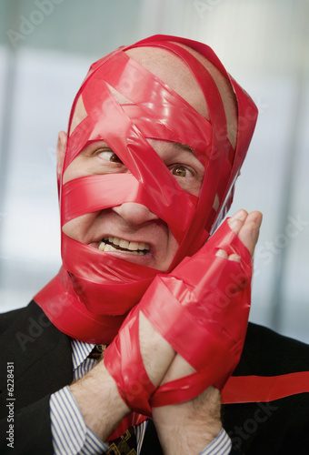 Cross-eyed businessman wrapped in red tape photo