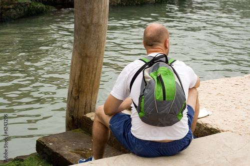 The hiker takes a rest on quay near the water