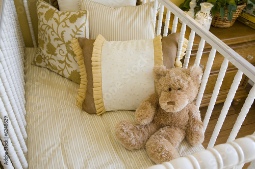 Baby bedroom with crib, pillows and a teddy bear.